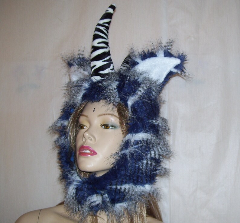 May include: A blue and white furry hooded hat with a zebra-print horn. The hat is worn by a mannequin with a neutral expression.