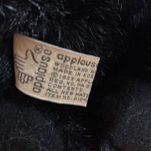 May include: A white tag with black text that reads "applause woodland n made in korea reg. no. pa 1988 applause contents all new materials item no. 212"