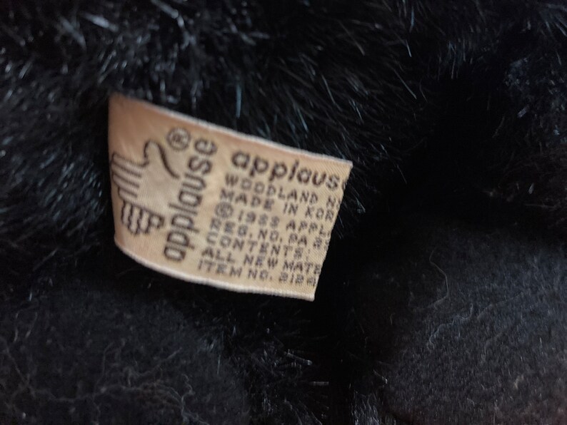 May include: A white tag with black text that reads "applause woodland n made in korea reg. no. pa 1988 applause contents all new materials item no. 212"