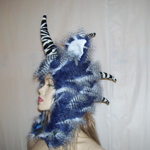 May include: A blue and white faux fur hat with a zebra-print horn and a white faux fur pom-pom on top.