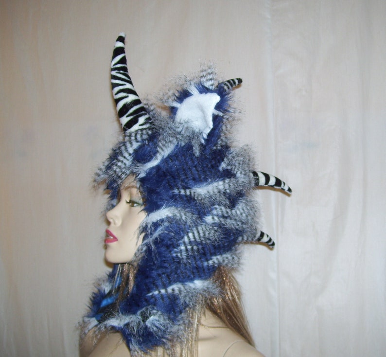 May include: A blue and white faux fur hat with a zebra-print horn and a white faux fur pom-pom on top.