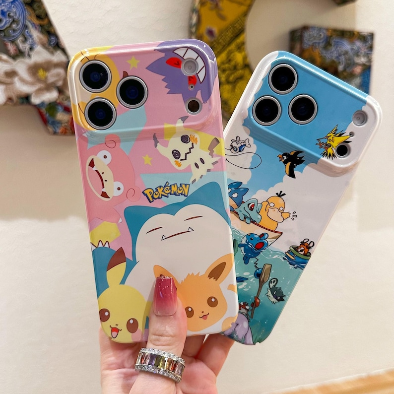 May include: Two colorful phone cases featuring Pok&eacute;mon characters. One case has a pink and purple background with Pikachu, Mimikyu, and Snorlax. The other case has a blue and white background with various water-type Pok&eacute;mon. The cases have a glossy finish.