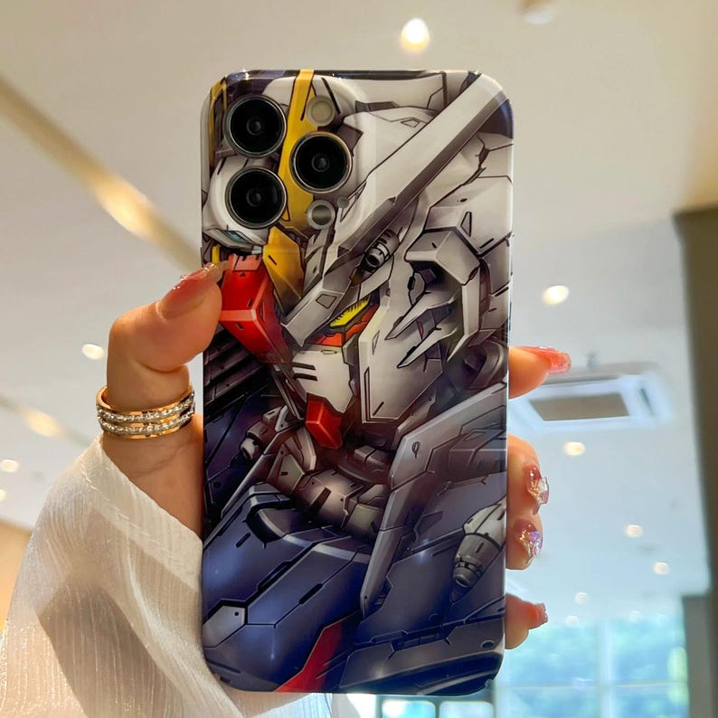 Pu&ograve; includere: Una custodia per telefono bianca e grigia con un design di personaggio anime colorato. Il personaggio ha un design rosso, giallo e blu. La custodia ha un ritaglio per la fotocamera con tre obiettivi.
