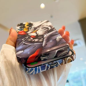 Pu&ograve; includere: Due custodie per telefono, una con un design di robot in stile anime colorato e l'altra con un design astratto blu e bianco.
