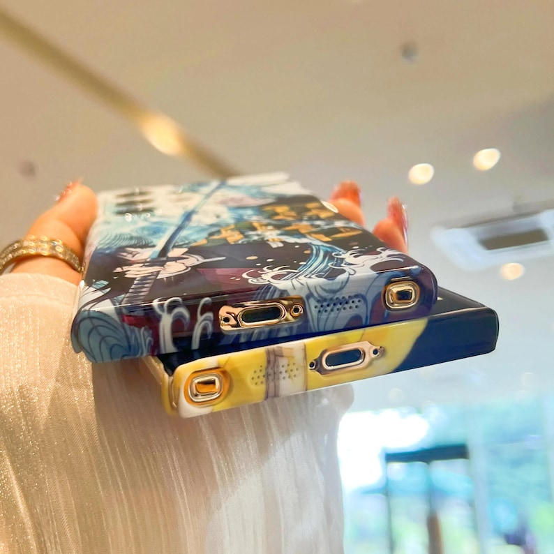 Pu&ograve; includere: Due custodie per telefono con un design anime colorato. La custodia superiore ha un design blu, bianco e nero con un bordo dorato. La custodia inferiore ha un design giallo, nero e bianco con un bordo dorato.