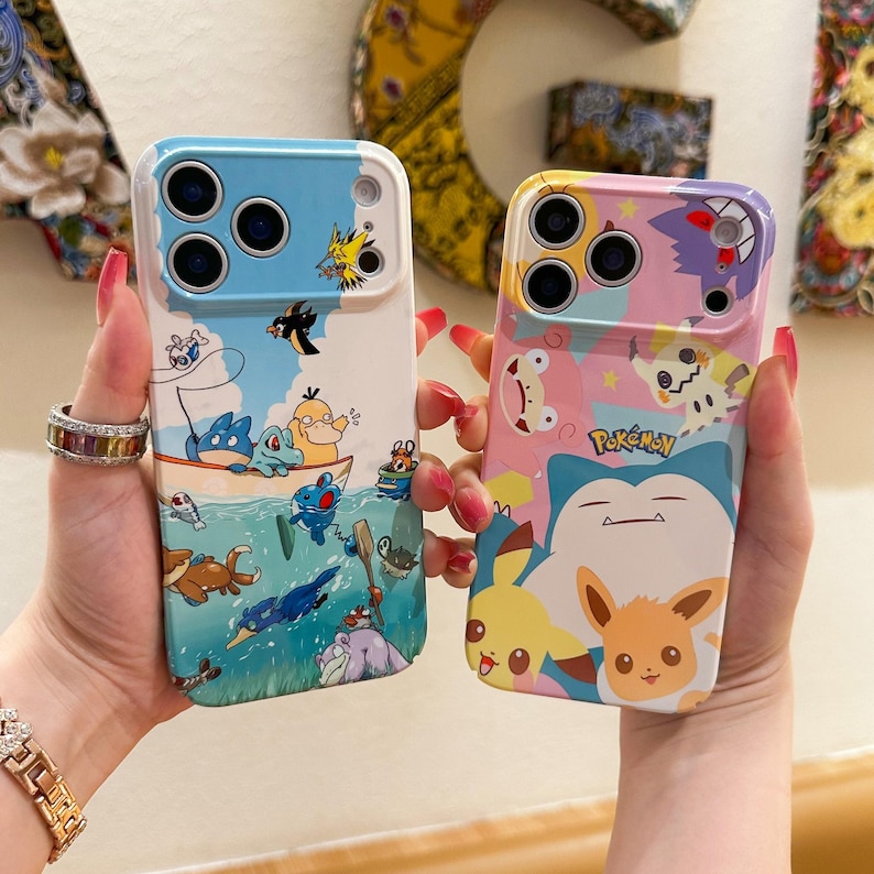May include: Two phone cases with colorful cartoon designs. One case features a blue and white design with cartoon characters in a boat. The other case has a pink and yellow design with Pokemon characters.