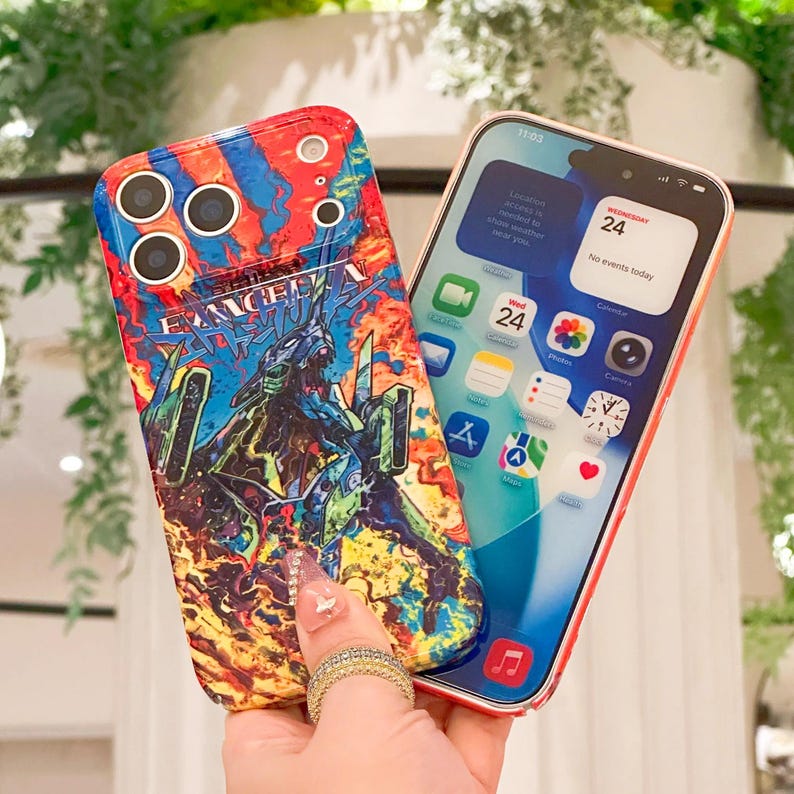 May include: A colorful phone case featuring a graphic design with the word "EVANGELION" and a character illustration. The case is held next to a smartphone displaying the date and time.
