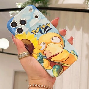 May include: A light blue phone case featuring a cartoon image of a yellow Psyduck character from the Pok&eacute;mon franchise. The case has a sunflower and sky design, with the word "Pok&eacute;mon" in blue.