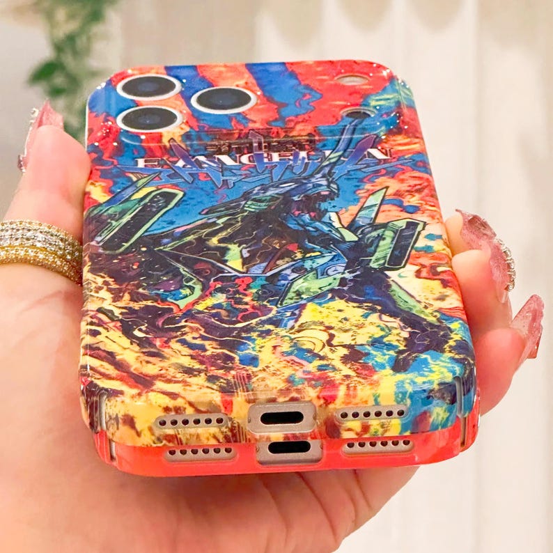 May include: A colorful phone case with a vibrant design featuring a detailed illustration. The case has a red border and a complex graphic with blue, green, and yellow hues. The text "EVANGELION" is visible on the case.