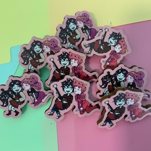 May include: A set of nine colourful cartoon character pins featuring a couple in various poses. The pins are made of wood and have a glossy finish.