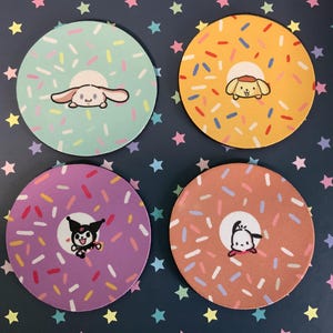 Puede incluir: Juego de cuatro posavasos redondos con personajes de dibujos animados y un diseño de donut. Cada posavasos tiene un fondo de color diferente: verde menta, amarillo, morado y naranja. Los posavasos están decorados con chispas de colores.