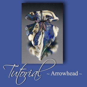 May include: A handcrafted glass arrowhead pendant with a blue, white, and cream color scheme. The pendant has a unique, organic shape with a textured surface and is tied with a dark cord and ribbon. The word "Tutorial" is written in cursive.