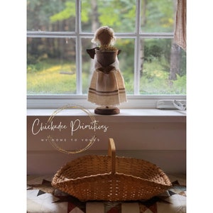 Puede incluir: Una cesta tejida con un asa de madera se encuentra sobre una colcha de retazos. La cesta es de color marrón claro y tiene una forma rectangular. La cesta está sobre una colcha de retazos con un diseño de retazos. El texto "Chickadee Primitives My Home to Yours" es visible en la imagen.