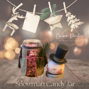 May include: A glass jar filled with red and white peppermint candies, wrapped in green plaid fabric with a red and white twine bow and a pine sprig. Beside it sits a round snowman head ornament wearing a black top hat.