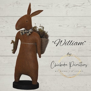May include: A brown felt bunny with a black and white checkered bow tie, carrying a basket of dried flowers. The bunny is standing on a black base. The text "William" and "Chickadee Primitives" is visible in the image.