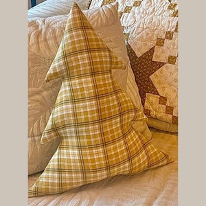 Peut inclure: Un oreiller en forme de sapin de Noël en plaid jaune et blanc. L'oreiller est posé sur une couverture de lit à motifs blancs et bruns.