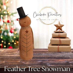 May include: A tan fabric snowman figurine wearing a black top hat and featuring a hand-drawn tree design with a star on its torso. Beside it is a stack of four brown paper-wrapped gifts topped with a gold star. Text reads Chickadee Primitives.
