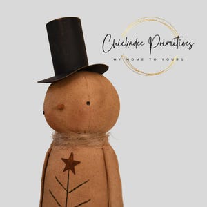 May include: A tan snowman doll wearing a black top hat, with a twig nose and a star and tree design on the front. The doll has a burlap scarf and the text "Chickadee Primitives" in the upper right corner.