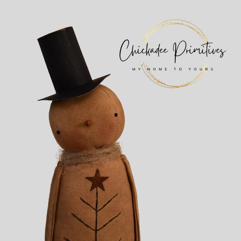 May include: A handmade snowman doll wearing a black top hat, a jute scarf, and a star and tree design on the front. The doll has a tan body and a round head with small black eyes and a button nose. The text "Chickadee Primitives" is in the background.