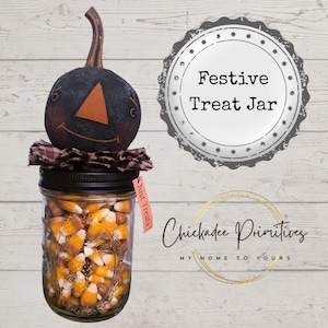 Könnte beinhalten: Ein dekoratives Glas gefüllt mit Zuckermais, gekrönt von einem schwarzen Kürbiskopf. Das Glas hat einen schwarzen Deckel und ein Etikett mit der Aufschrift "Just Treats!". Das Bild enthält auch den Text "Festive Treat Jar".