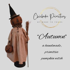 May include: A handmade primitive pumpkin witch doll wearing a brown dress, a black hat, and holding a broom. The doll is carrying a small pumpkin. The text "Autumn" is written in cursive above the doll.