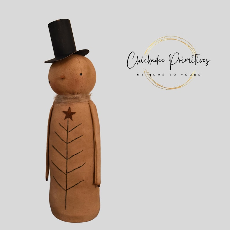 May include: A handcrafted, tan-coloured doll with a black top hat and a star and tree design. The doll has a rustic, primitive aesthetic, with a simple face and a neutral colour palette. The doll is approximately 30 cm tall.