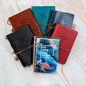 May include: A collection of six leather-bound journals with compass designs and a clear journal with the text "My Dive Log Story".
