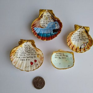 May include: Four painted scallop shells with gold edging, each bearing a different inspirational quote. One shell depicts a lighthouse scene. The text includes verses from John and Revelation.