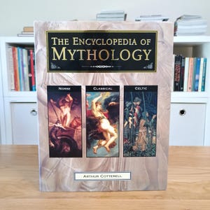 May include: A hardback book titled The Encyclopedia of Mythology by Arthur Cotterell. The cover features a black rectangular title box and three vertical panels depicting Norse, Classical, and Celtic mythological scenes in a beige background.