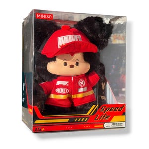 May include: A plush Mickey Mouse toy in a clear plastic box. Mickey is wearing a red cap and jacket with yellow stripes. The box has the text "MINISO" and "Speed Life". The toy is suitable for ages 15+.