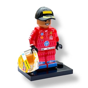 Może przedstawiać: Figurka Lego kierowcy Formuły 1 w czerwonym kombinezonie wyścigowym, czapce i z kaskiem. Figurka stoi na czarnej podstawie. Kask jest żółto-biały z logo sponsorów. Kombinezon ma numer 44.