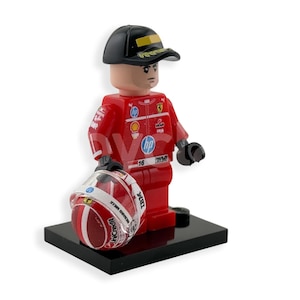 Könnte beinhalten: Eine Lego-Figur eines Formel-1-Fahrers in rotem Rennanzug und schwarzer Kappe, die einen Rennhelm hält. Der Helm ist rot und weiß mit Sponsorenlogos. Die Figur steht auf einer schwarzen Basis.