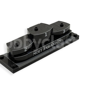 Könnte beinhalten: Schwarzes Plastikpodest mit drei Stufen, nummeriert 1, 2 und 3. Die Basis des Podests trägt den Schriftzug "Moët & Chandon".