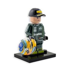 Puede incluir: Una figura de Lego de un piloto de Fórmula 1 con un traje y gorra de carreras verdes y negros. La figura sostiene un casco amarillo y azul. La figura está sobre una base negra.