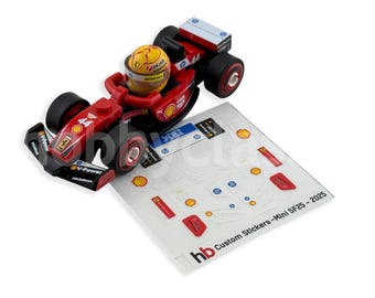 May include: A red and black toy race car with the number 44 and a yellow helmeted driver. The car has sponsor logos and sits next to a sheet of custom stickers with the text "hb Custom Stickers - Mini SF25-2025".