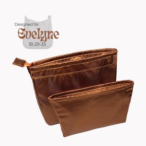 May include: Two brown satin pouches, one larger than the other, are displayed against a white background. The pouches have a drawstring closure and a small tab on the side. The text "Designed for Evelyne 18-29-33" is in the upper left corner.
