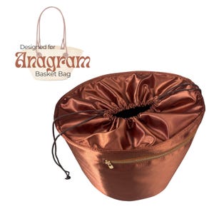 May include: A brown satin drawstring bag with a gold zip, designed for the Anagram Basket Bag. The bag has a drawstring closure and a matching brown cord. The text "Designed for Anagram Basket Bag" is visible.