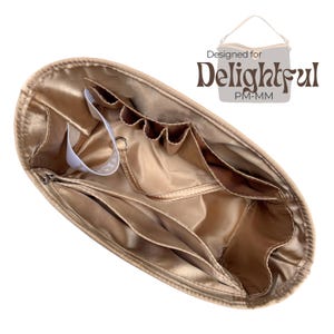 Könnte beinhalten: Goldfarbener Handtaschen-Organizer mit mehreren Taschen und Fächern. Der Organizer hat einen Reißverschluss und ein weißes Etikett. Der Text "Designed for Delightful PM-MM" ist oben rechts sichtbar.