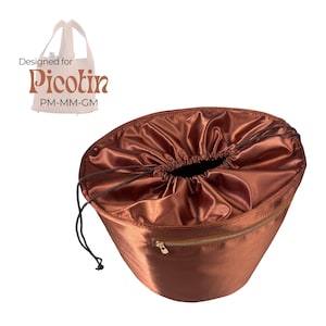 May include: A brown satin bag with a drawstring closure and a gold zipper. The bag is designed for a Picotin bag. The text "Designed for Picotin" is visible in the image.