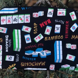 May include: A black Mahjong-themed zippered pouch featuring a repeating pattern of Mahjong tiles, dice, and Chinese characters. The design includes the words "BAM", "BAMBOO", "SUMMER", and "WINTER". The pouch is rectangular and appears to be made of fabric.