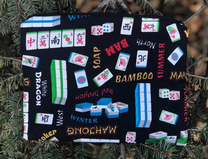 May include: A black Mahjong-themed zippered pouch featuring a repeating pattern of Mahjong tiles, dice, and Chinese characters. The design includes the words "BAM", "BAMBOO", "SUMMER", and "WINTER". The pouch is rectangular and appears to be made of fabric.