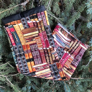 May include: A black drawstring bag with a book print design. The print features a variety of colourful books with gold accents.