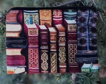 May include: A black zippered pouch with a colorful print of stacked books with gold accents. The books have various titles and decorative designs.
