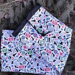 May include: A black drawstring bag with a white background and a pattern of mahjong tiles. The tiles are printed with Chinese characters and numbers. The bag is made of a durable fabric and has a drawstring closure.