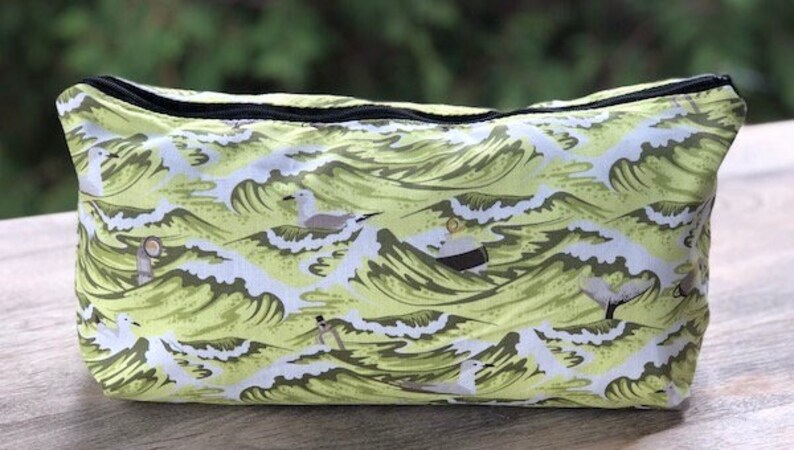 May include: A green and white zippered pouch with a pattern of waves and seagulls.