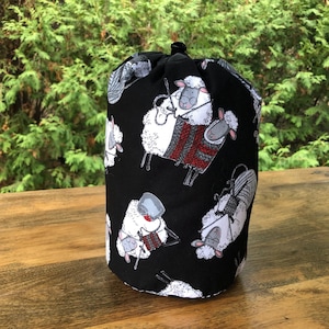 May include: Black drawstring bag with a white sheep pattern. The sheep are knitting and holding yarn balls.