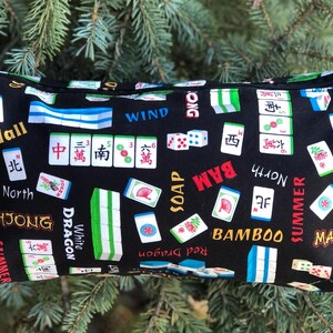 Puede incluir: Bolsa negra con cremallera con un dise&ntilde;o de fichas de Mahjong. El dise&ntilde;o incluye fichas, dados y caracteres chinos en rojo, verde, blanco y azul. Tambi&eacute;n son visibles las palabras "Mahjong", "Bamboo" y "Summer".