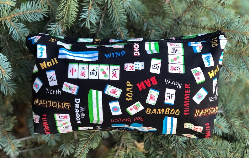 Puede incluir: Bolsa negra con cremallera con un dise&ntilde;o de fichas de Mahjong. El dise&ntilde;o incluye fichas, dados y caracteres chinos en rojo, verde, blanco y azul. Tambi&eacute;n son visibles las palabras "Mahjong", "Bamboo" y "Summer".