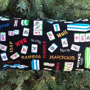 Puede incluir: Bolsa rectangular negra con cremallera y un estampado de fichas de Mahjong. La bolsa presenta varias fichas de Mahjong, dados y texto como "BAM", "North" y "Mahjong". El fondo es negro y el ribete es verde.