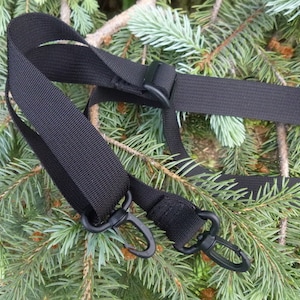 May include: Black adjustable strap with two black metal clips. The strap is made of a woven nylon material.